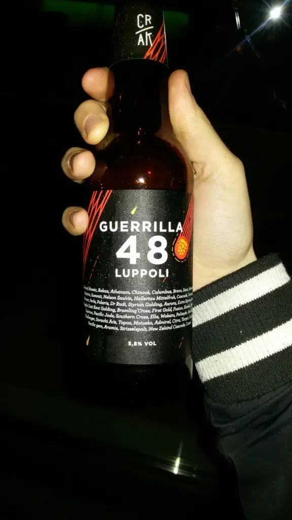 Mano che tiene una bottiglia di birra del birrificio Crak dal nome Guerilla 48 luppoli.